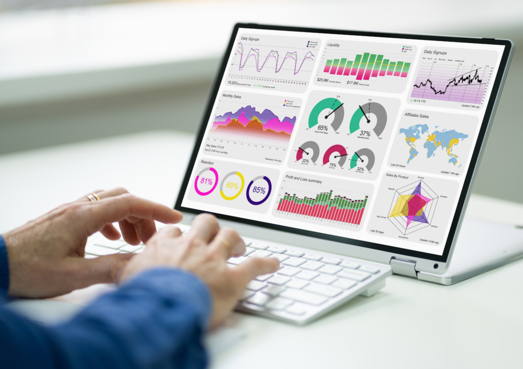 A person using a laptop with a screen displaying various colorful data visualizations, including bar graphs, pie charts, line graphs, and maps. The visualizations represent metrics related to sales, performance, and customer engagement, while the person's hands are positioned on the keyboard, suggesting active interaction with the data.